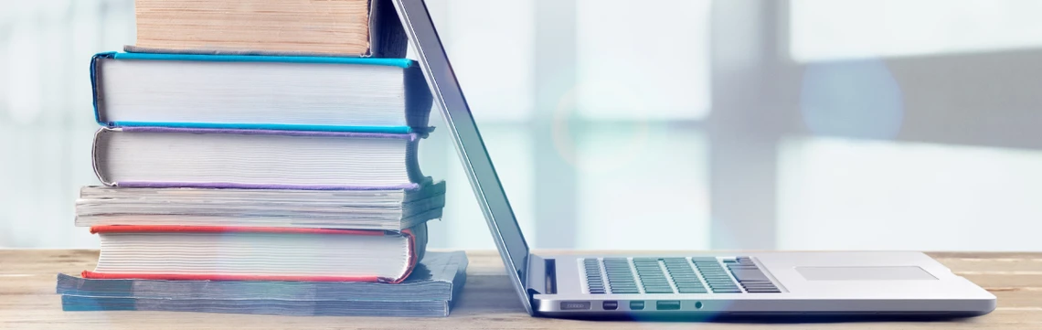Various books stacked up against an open laptop