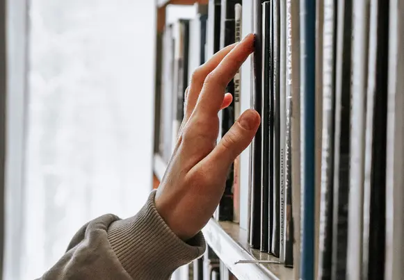 Person's hand searching stacks for a specific book