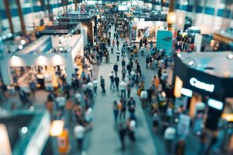 Crowded trade show with multiple exhibition booths and visitors.