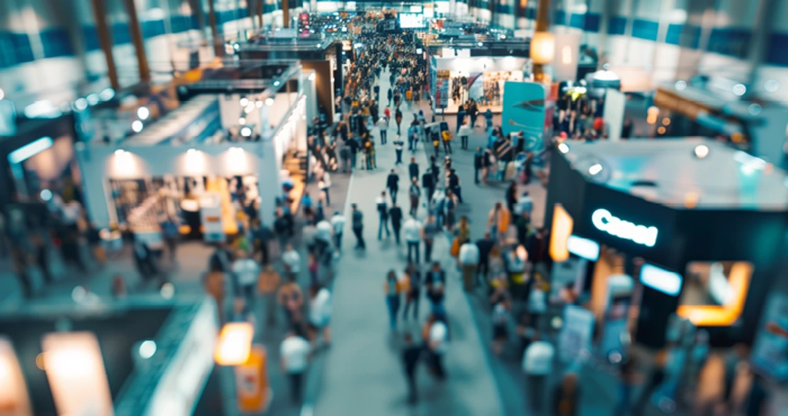 Crowded trade show with multiple exhibition booths and visitors.