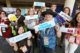A group of people holding signs related to libraries at ALA Annual