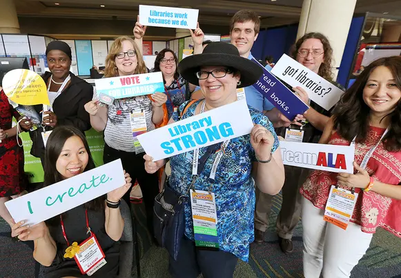 A diverse group of nine people holding signs promoting libraries at a conference.