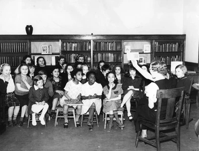 Children sitting on chairs in a library listening to a librarian tell a story